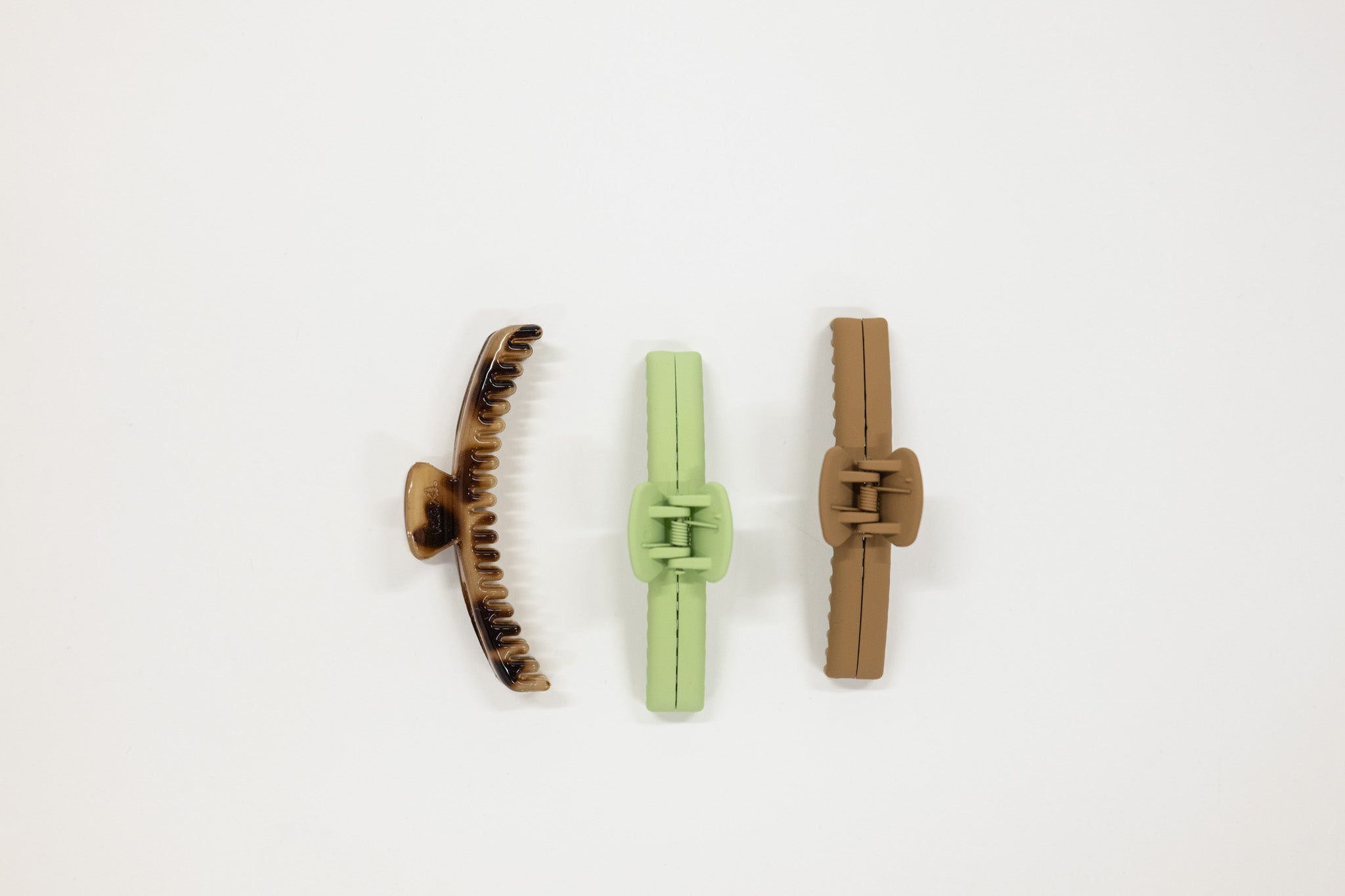 Three hair clips in brown, green, and beige on a white background
