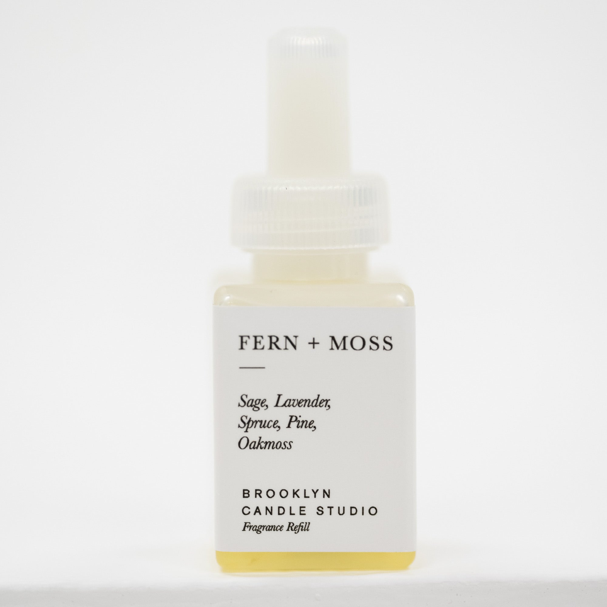 A small square bottle of Fern + Moss Pura Fragrance Refill by Brooklyn Candle Studio, featuring a white label and a translucent white dropper cap, containing a pale yellow liquid.