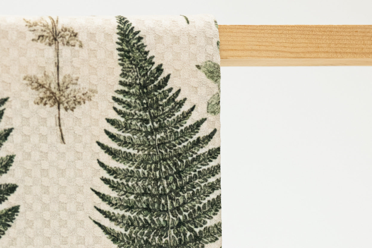 Towel with fern leaf pattern hanging on a wooden rod against a light background