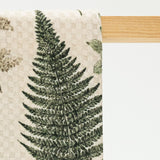 Towel with fern leaf pattern hanging on a wooden rod against a light background
