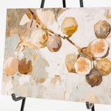 An abstract botanical painting of fruit branches with cream, tan, brown, and muted green tones, displayed on a black easel against a white background.