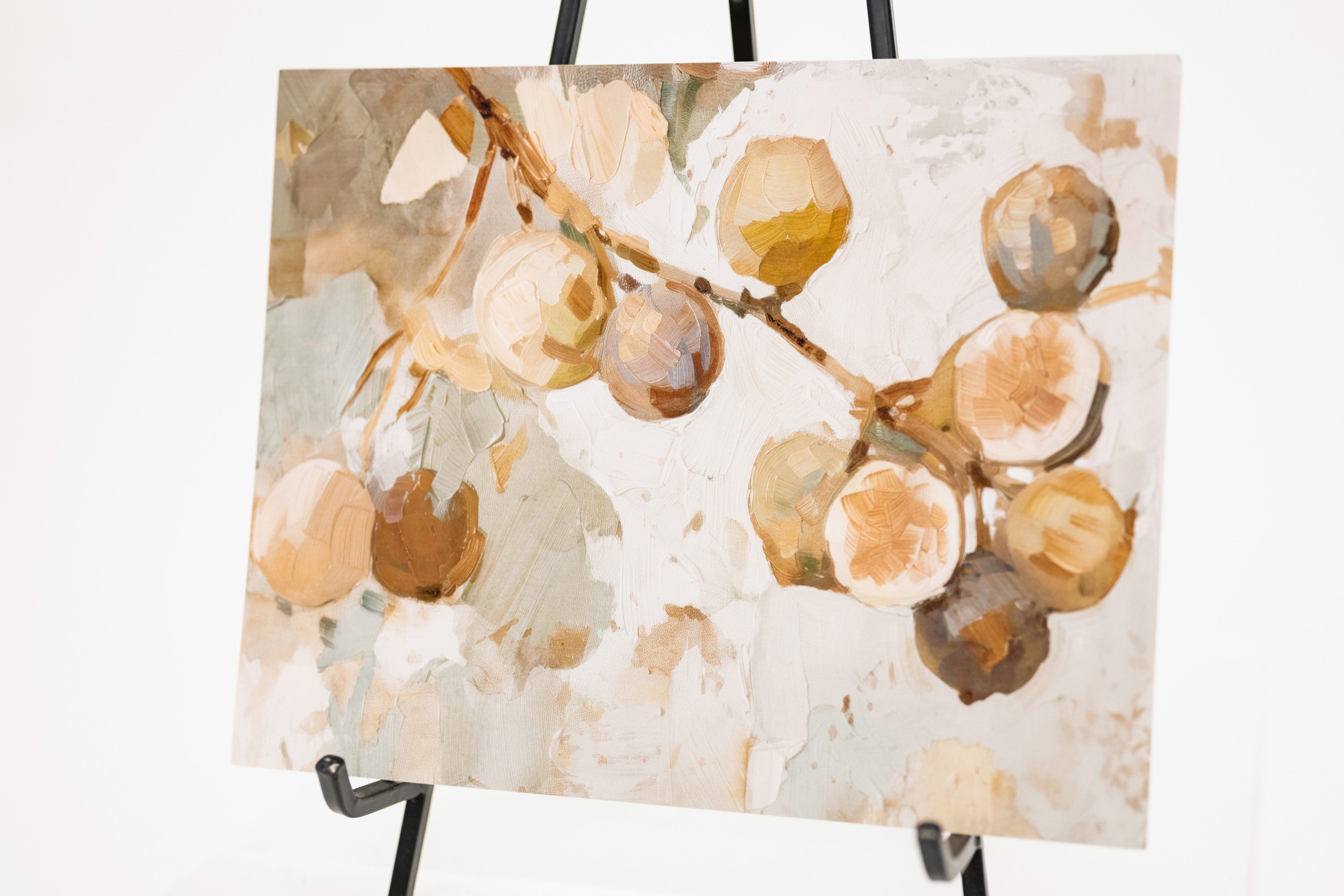 An abstract botanical painting of fruit branches with cream, tan, brown, and muted green tones, displayed on a black easel against a white background.