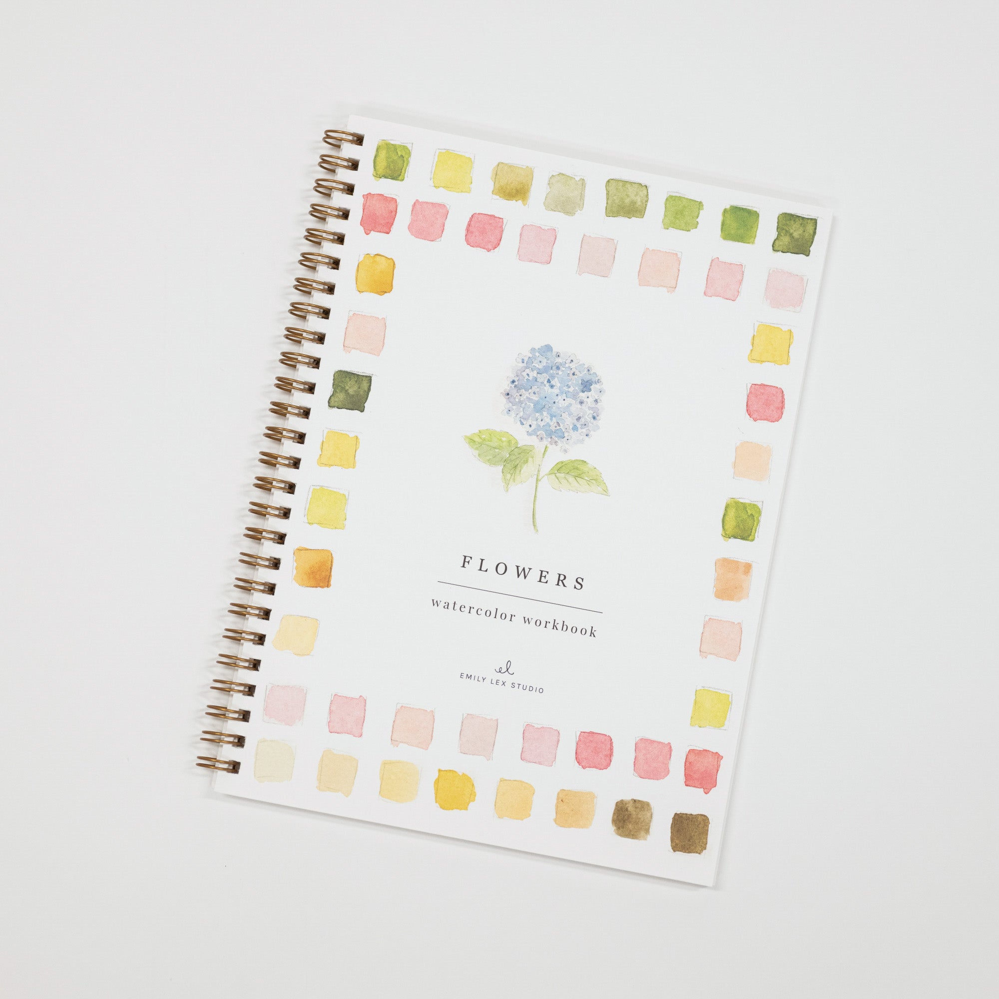 A spiral-bound watercolor notebook titled 'FLOWERS watercolor workbook' with a white cover, featuring a central blue hydrangea illustration and a border of small pastel watercolor squares in pink, yellow, green, and peach. The notebook is photographed at an angle on a light gray background.