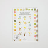 A spiral-bound notebook titled 'learn to paint with watercolor' by Origami Design, featuring a white cover decorated with watercolor flower illustrations and color swatches, shown on a light gray background.