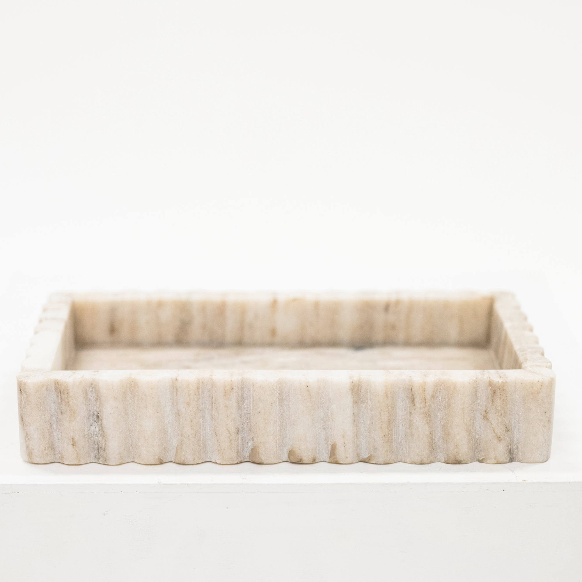A beige marble tray with fluted sides.