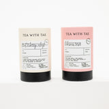 Two cylindrical tea packaging tubes standing upright on a white background. The left tube is cream with a black base and reads 'TEA WITH TAE' and 'fruit & berry notes.