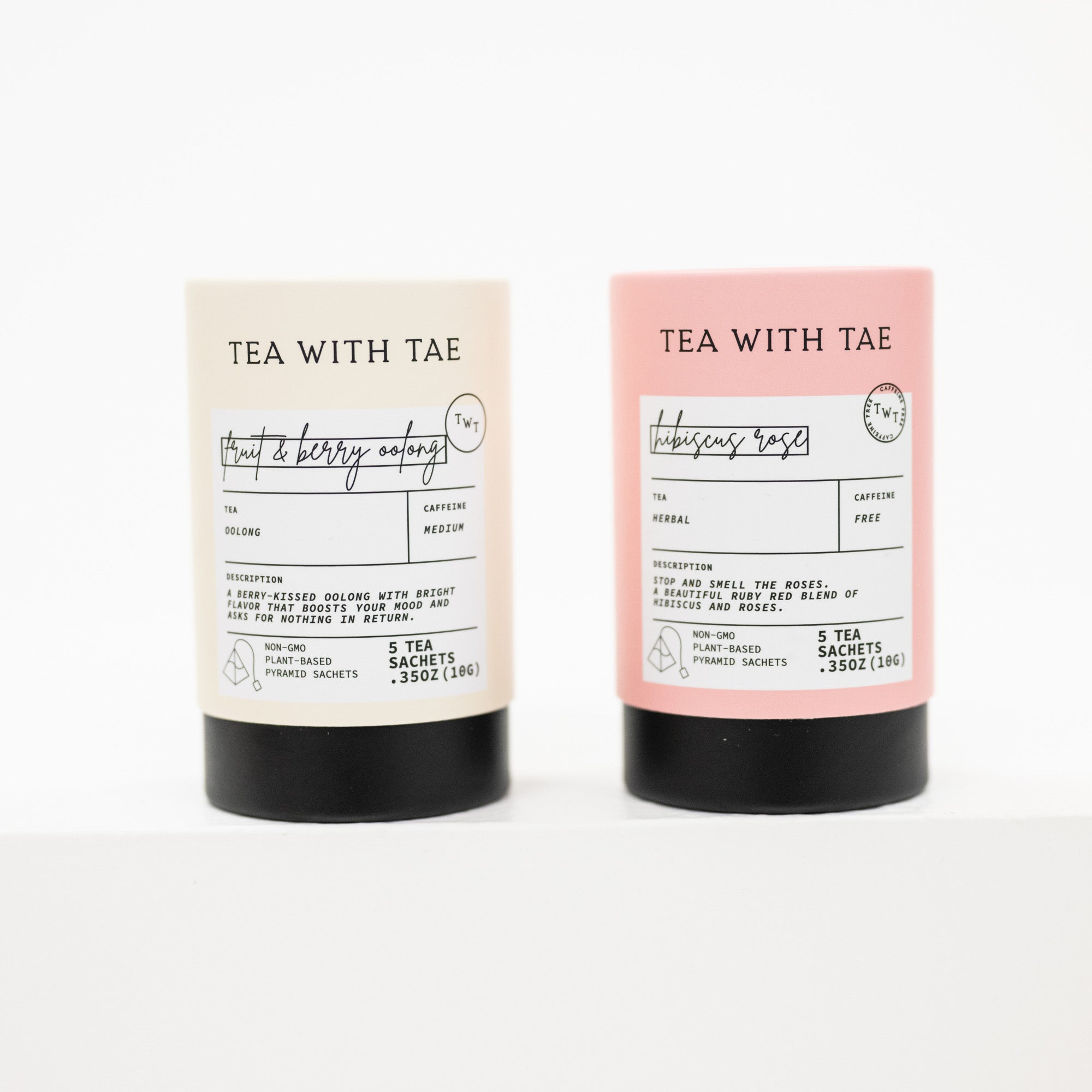 Two cylindrical tea packaging tubes standing upright on a white background. The left tube is cream with a black base and reads 'TEA WITH TAE' and 'fruit & berry notes.