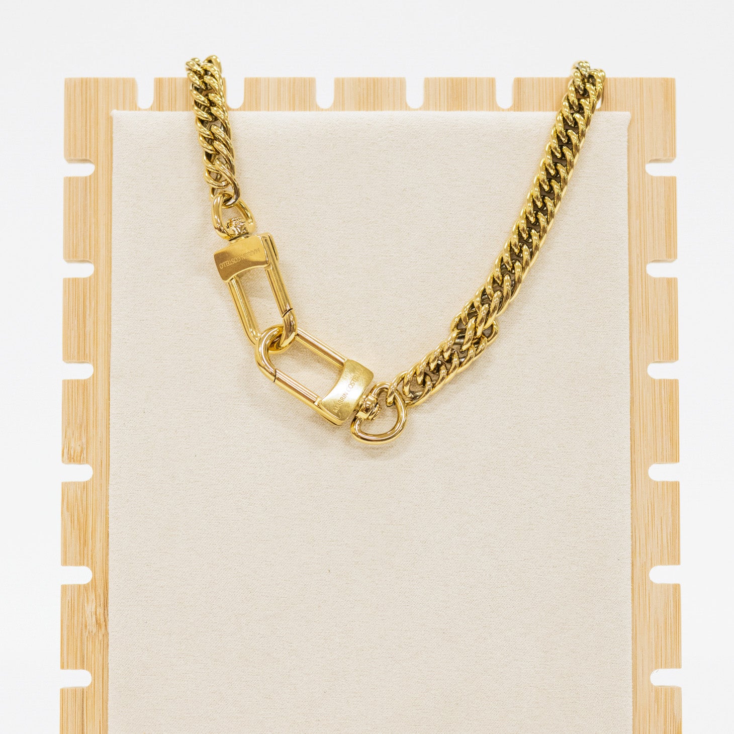 Gold chain necklace on a wooden stand with a white background