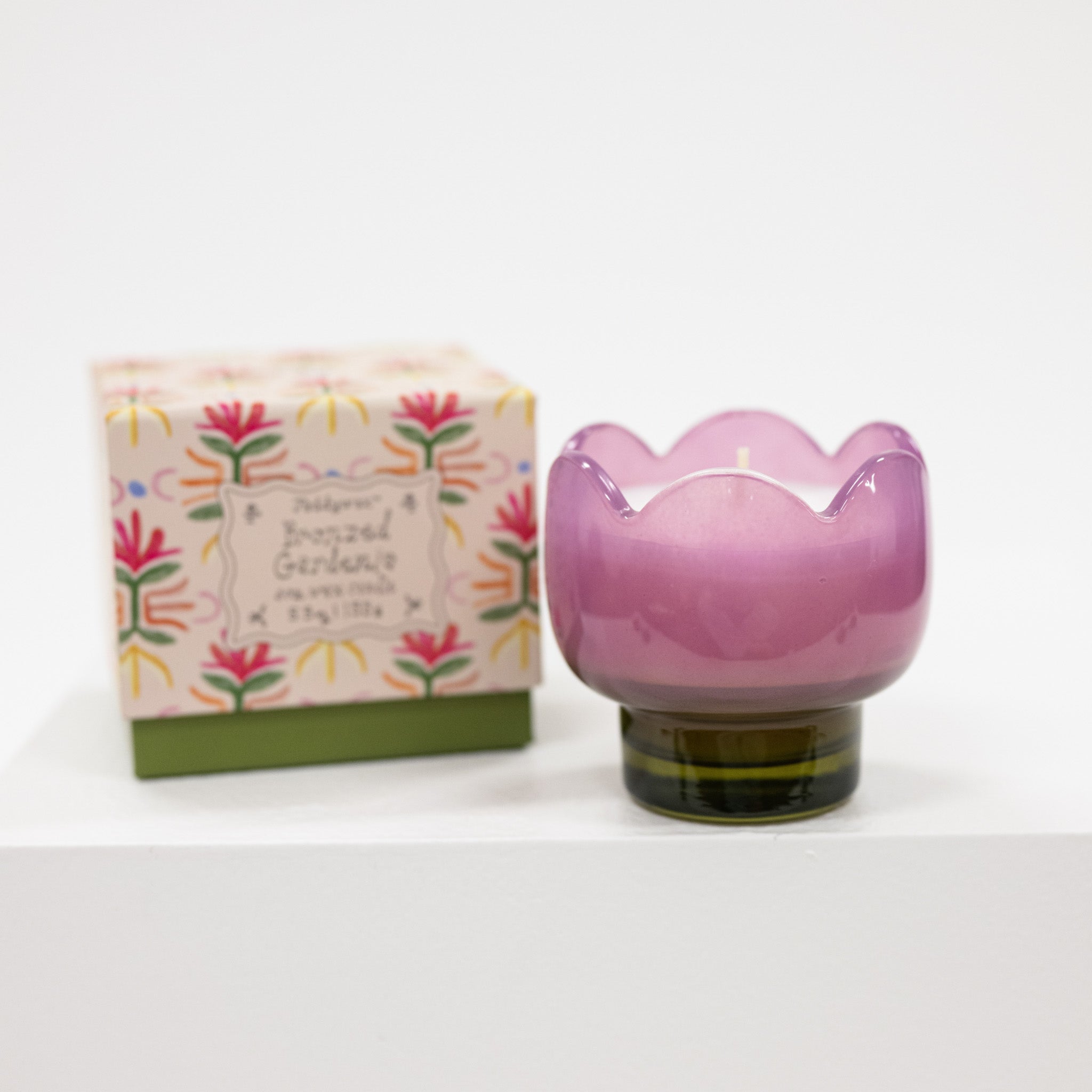 Pink glass candle holder with floral packaging on a white background