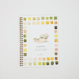 A spiral-bound watercolor workbook titled 'GARDEN' with a white cover, surrounded by a border of small watercolor paint swatches in green, yellow, orange, and pink. The cover also features a delicate illustration of potted plants in the center.