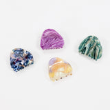Four hair claw clips made from natural abalone shells, displayed on a clean white background. The clips feature marbled patterns in purple, green, blue, and yellow.