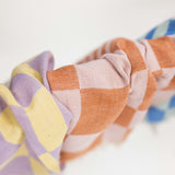 A close-up of a woven kitchen towels with a soft checkered pattern in pastel orange, pink, and lavender, with a hint of a blue in the background.