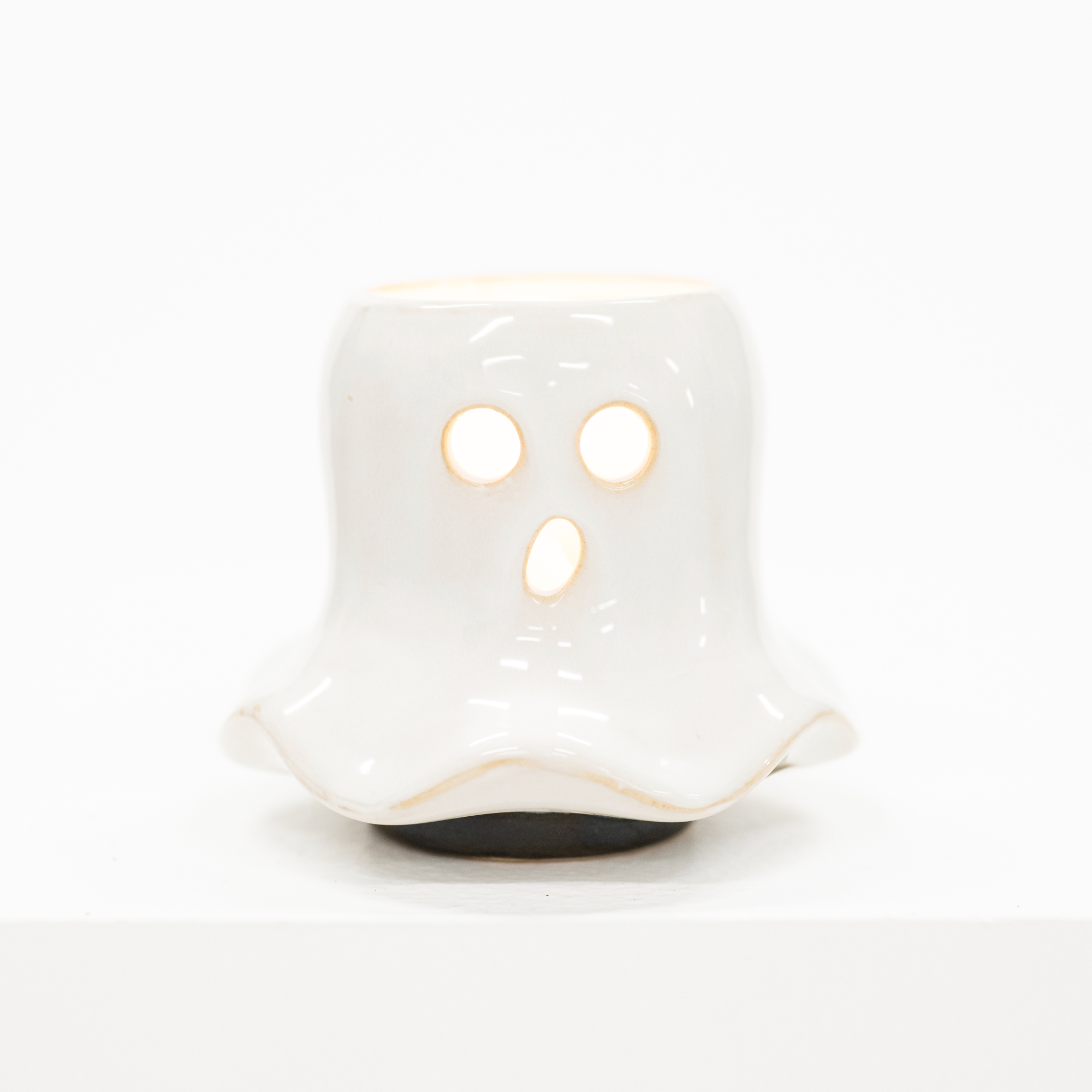 A small white ghost-shaped ceramic candle holder with cutout eyes and mouth, shown on a clean white background.