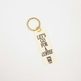 A rectangular cream-colored acrylic keychain with the text 'LET'S GO FOR A COFFEE' in black lettering and a small coffee cup graphic, attached to a gold split ring, shown on a plain white background.