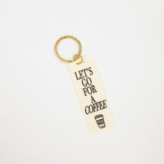 A rectangular cream-colored acrylic keychain with the text 'LET'S GO FOR A COFFEE' in black lettering and a small coffee cup graphic, attached to a gold split ring, shown on a plain white background.