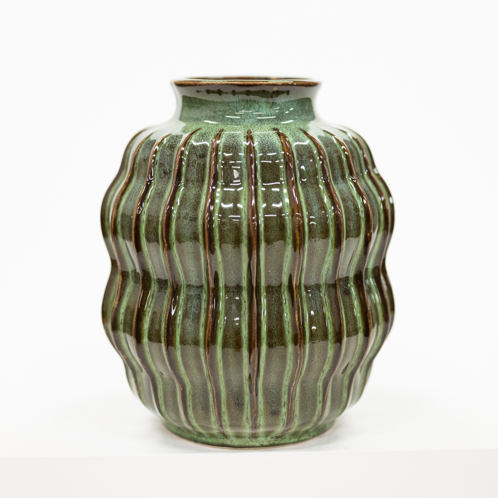 A ribbed ceramic vase with a glossy green and brown glaze, photographed against a clean white background.