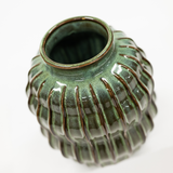 A small ribbed ceramic vase with a glossy green glaze and dark brown edging, shown on a plain white background.