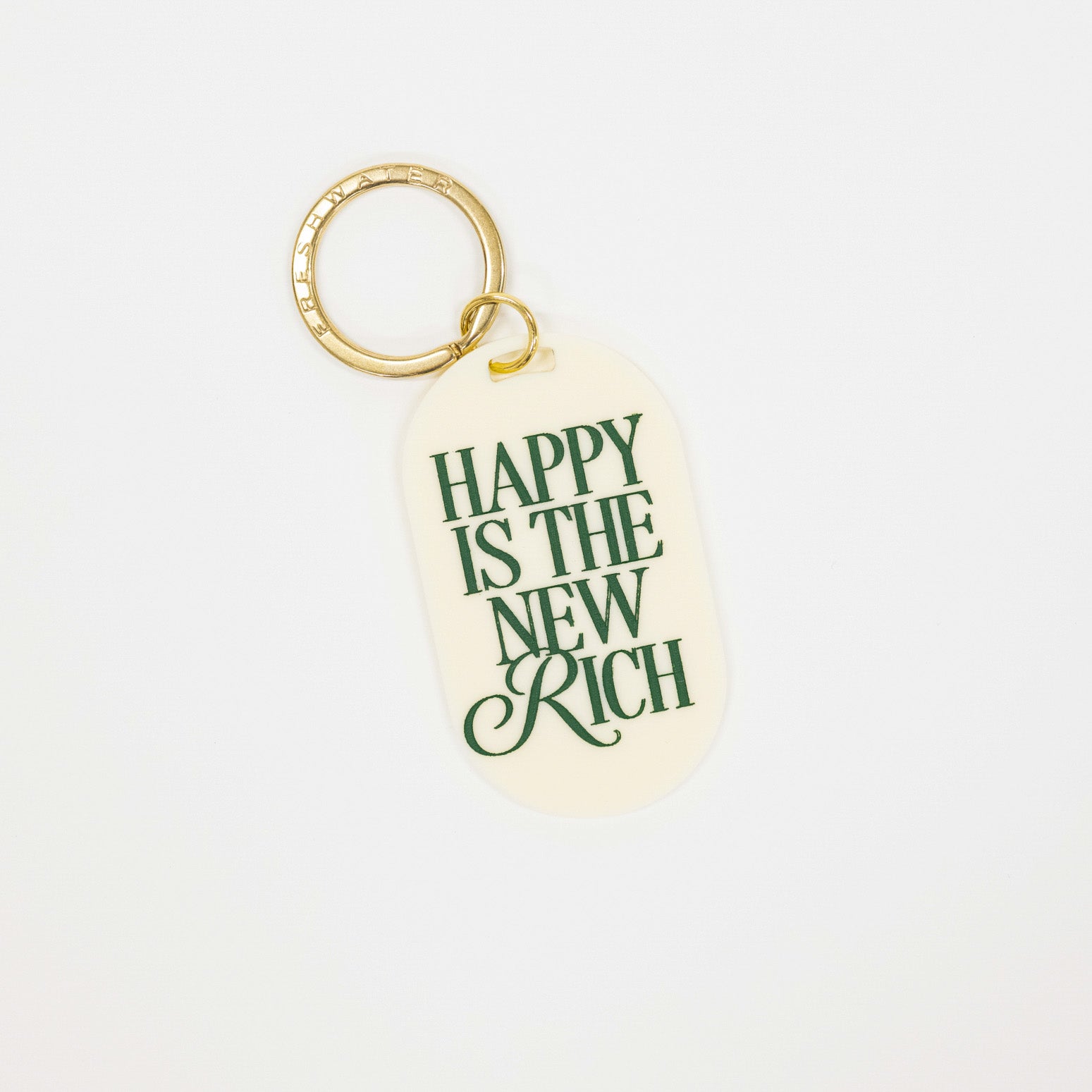 cream colored acrylic oval shaped keychain with the phrase "happy is the new rich" written in forest green. on a gold metal keychain loop