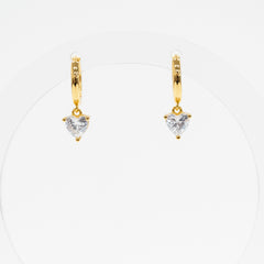 A pair of gold huggie hoop earrings with a small heart-shaped clear gemstone dangling from the center, displayed on a clean white background.