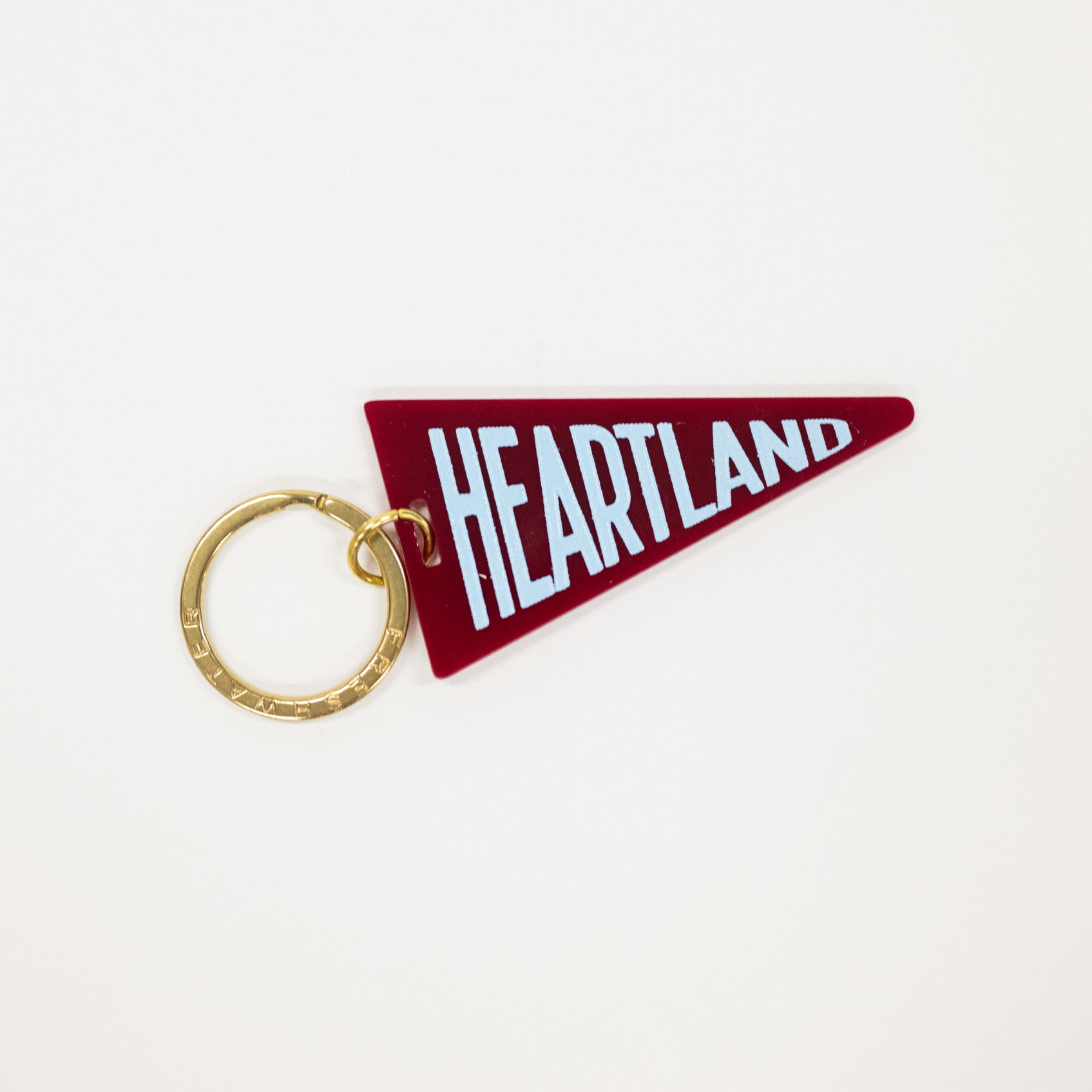 A heart-shaped red keychain featuring the word 'HEARTLAND' in white block letters, attached to a gold split key ring, shown on a plain white background.
