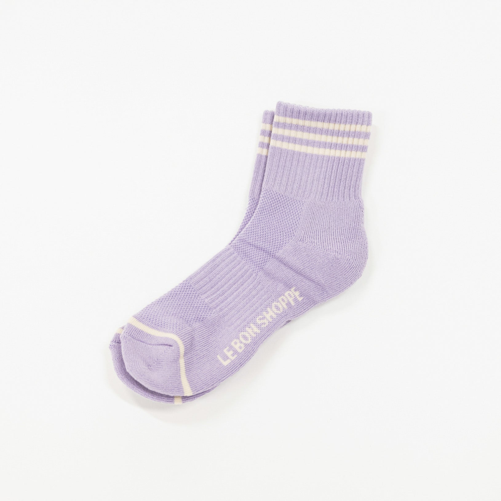 A single light purple crew sock with light yellow stripes at the ribbed cuff and a light yellow toe cap, featuring the text 'LE BON SORCIÈRE' printed on the side, shown on a plain white background.