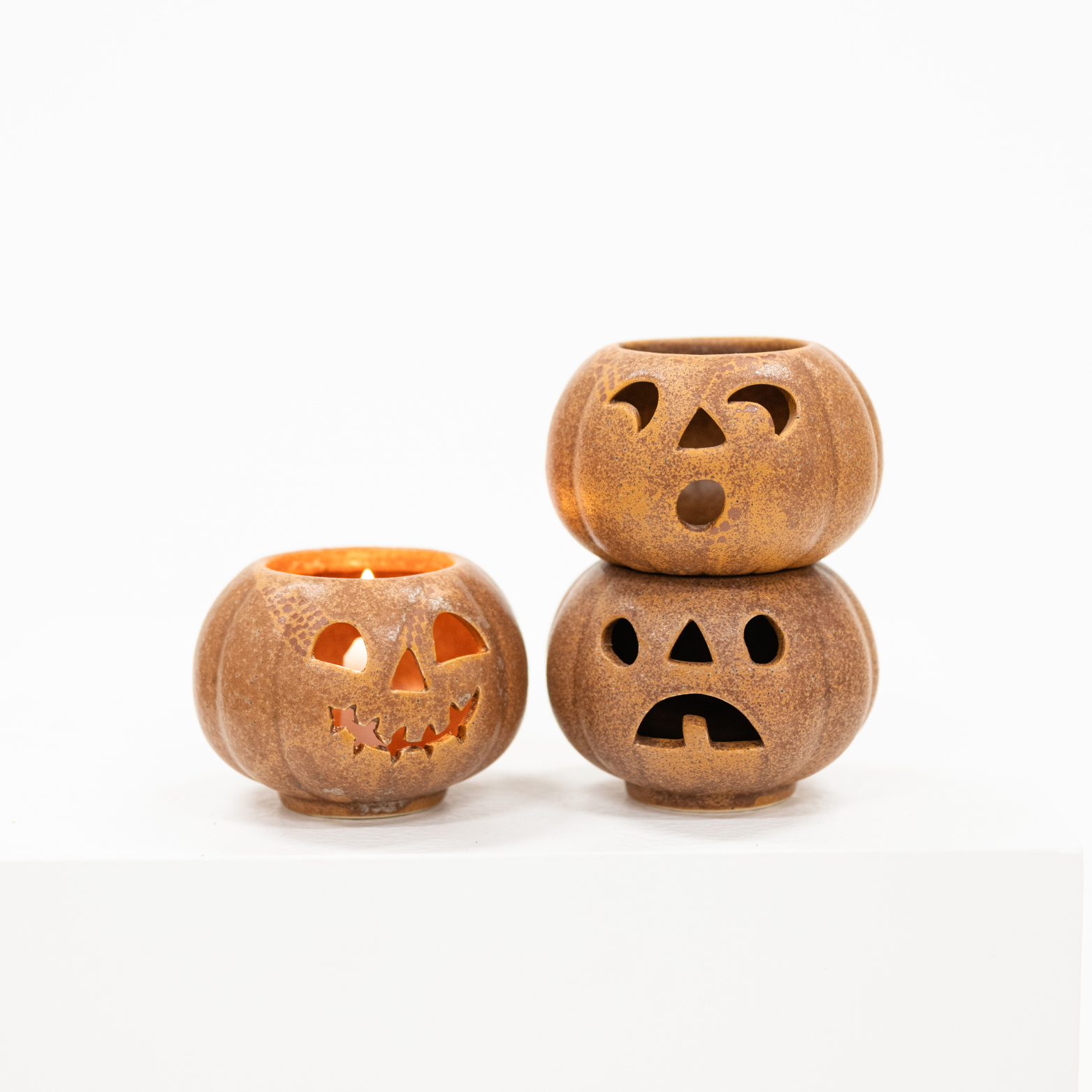 Three small pumpkin-shaped candle holders with carved jack-o'-lantern faces, arranged on a white surface against a white background.