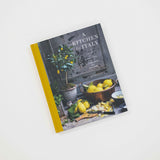 A hardcover cookbook titled "A Kitchen in Italy" photographed on a clean white background. The book has a mustard yellow spine and cover border, with a dark photographic scene on the front featuring lemons, a bowl, and kitchen elements.