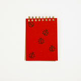 A small red spiral-bound notebook with black ladybug illustrations on the cover, photographed on a plain white background.