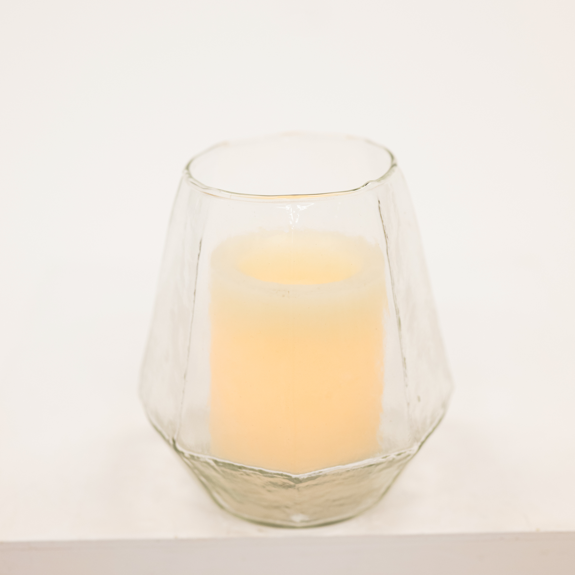 Clear glass candle holder with a lit candle on a white background
