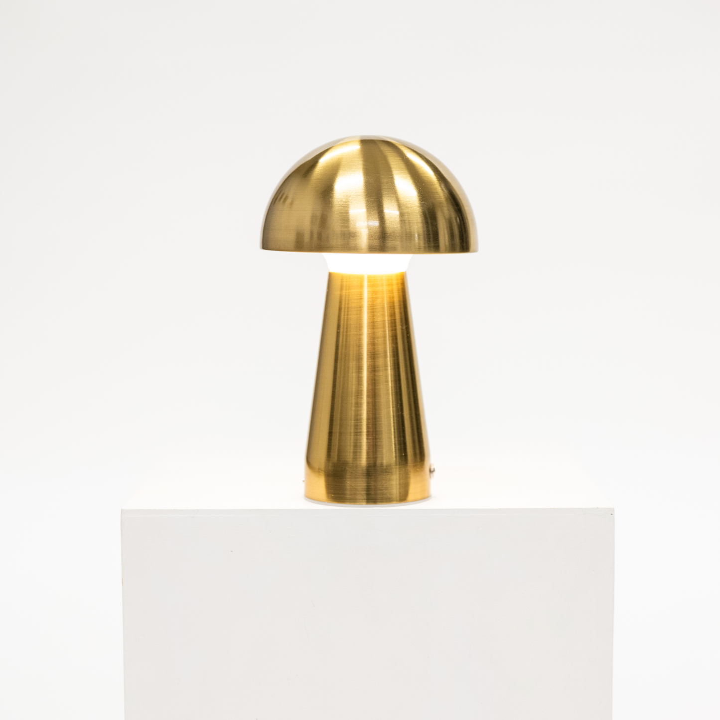 Gold table lamp on a white pedestal against a white background