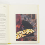 Open cookbook showing a page with text and an image of pizzas on a stone oven.