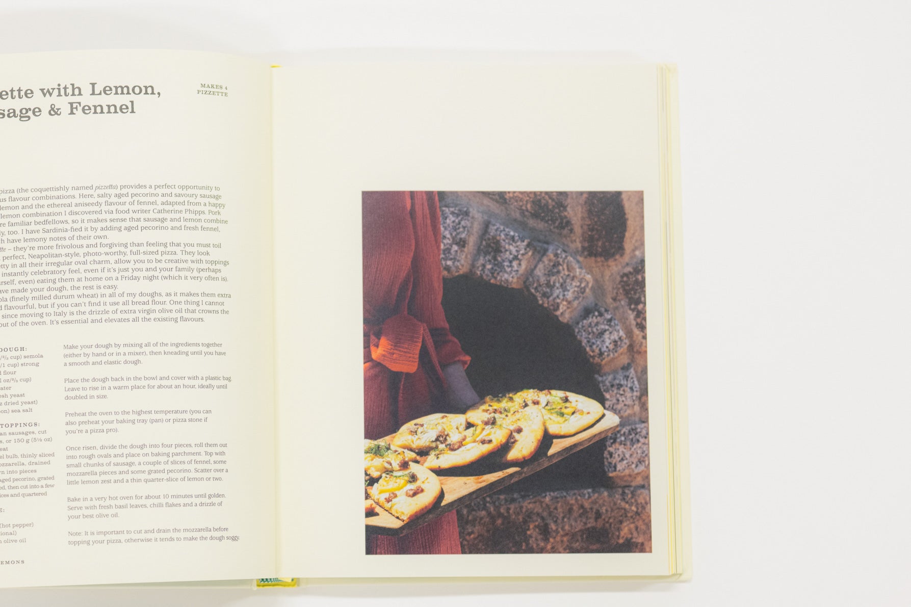 Open cookbook showing a page with text and an image of pizzas on a stone oven.