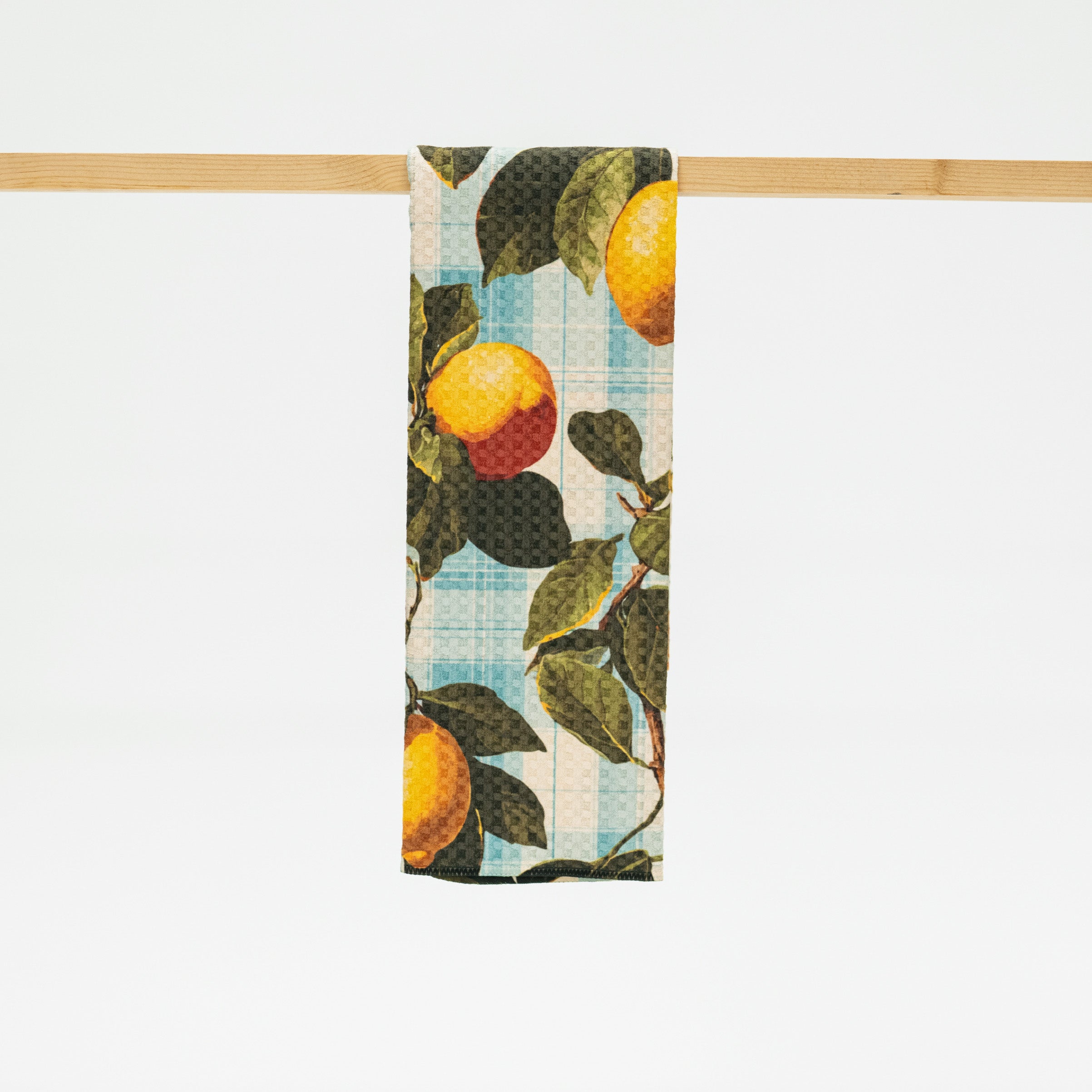 Towel with lemon and leaf pattern hanging on a wooden rod against a white background