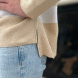 Close-up of a person wearing a beige sweater and light blue jeans.