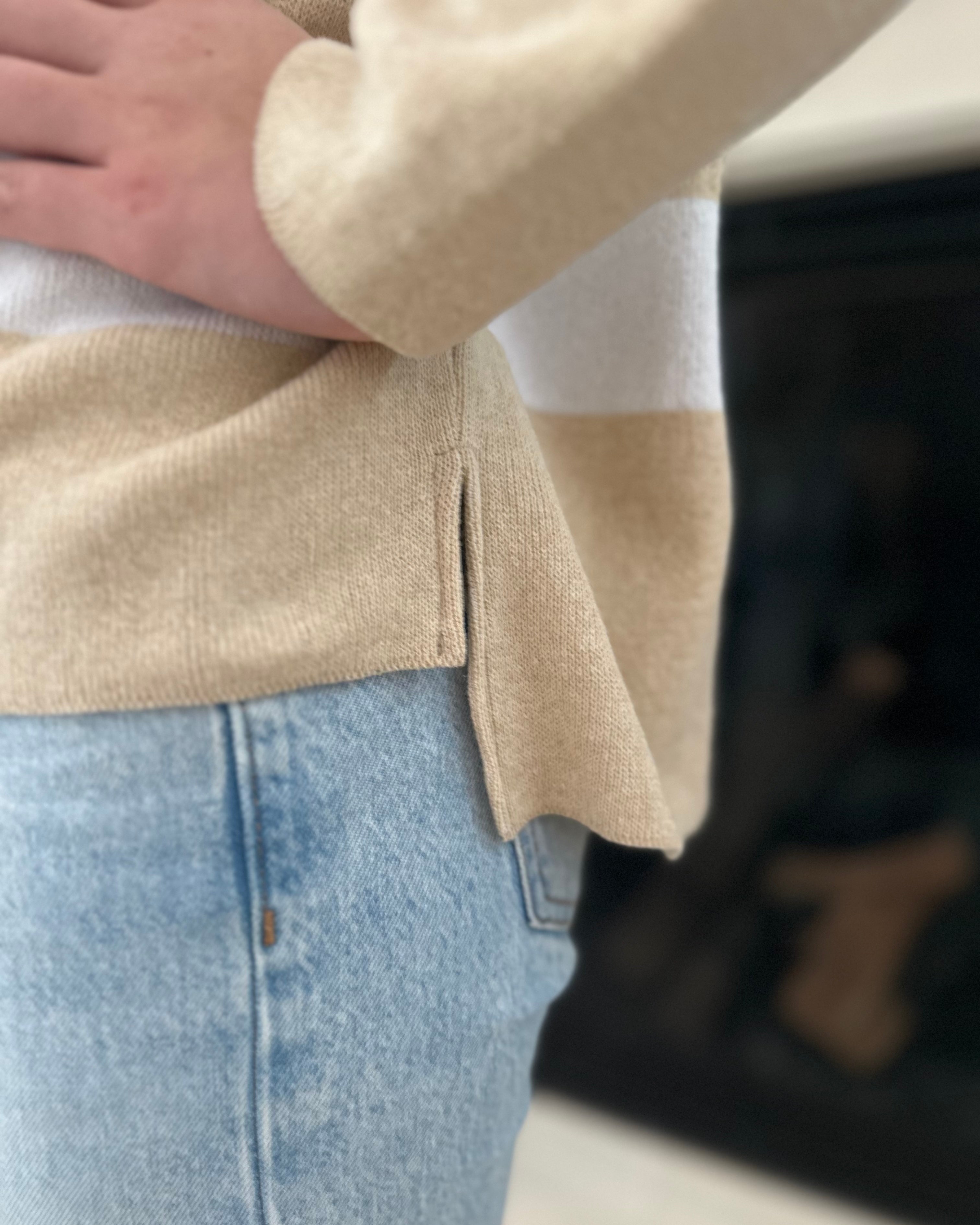 Close-up of a person wearing a beige sweater and light blue jeans.