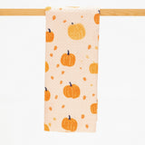 A fabric kitchen towel with an orange pumpkin and acorn pattern on a light peach background, hanging from a wooden dowel against a white background.