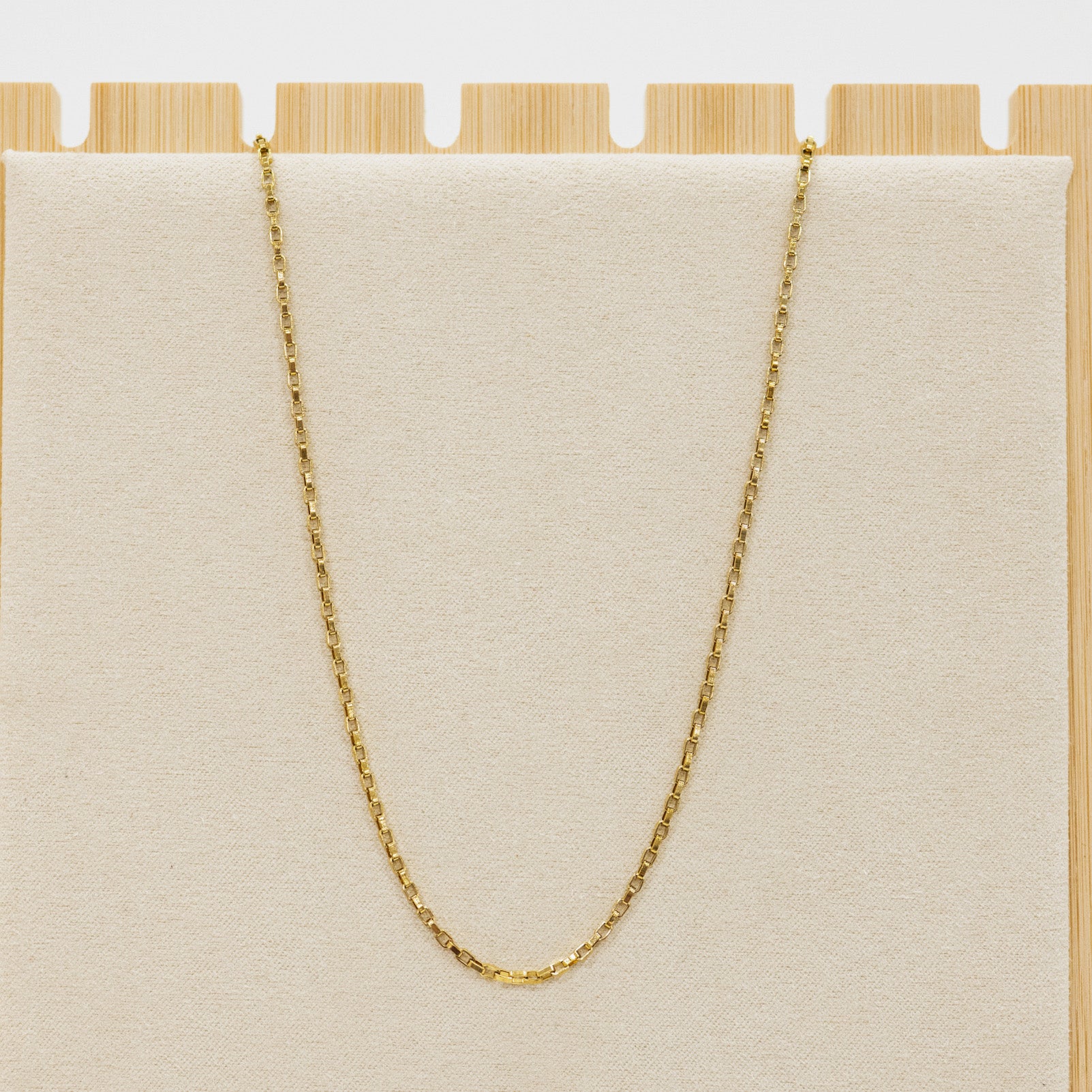 Gold chain necklace on a beige cushion with a wooden base