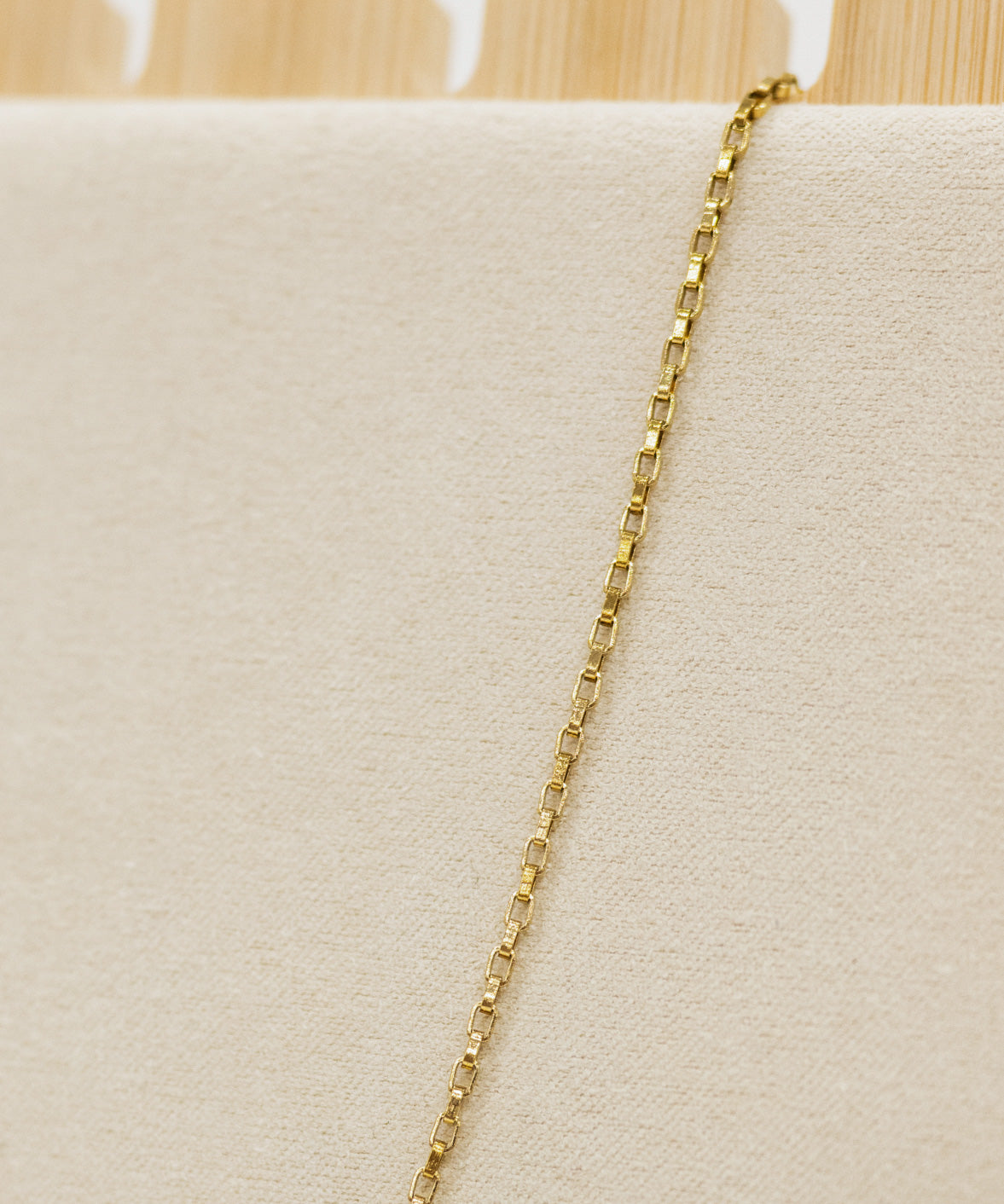 Gold chain necklace on a beige cushion with a wooden stand in the background