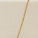 Gold chain necklace on a beige cushion with a wooden stand in the background
