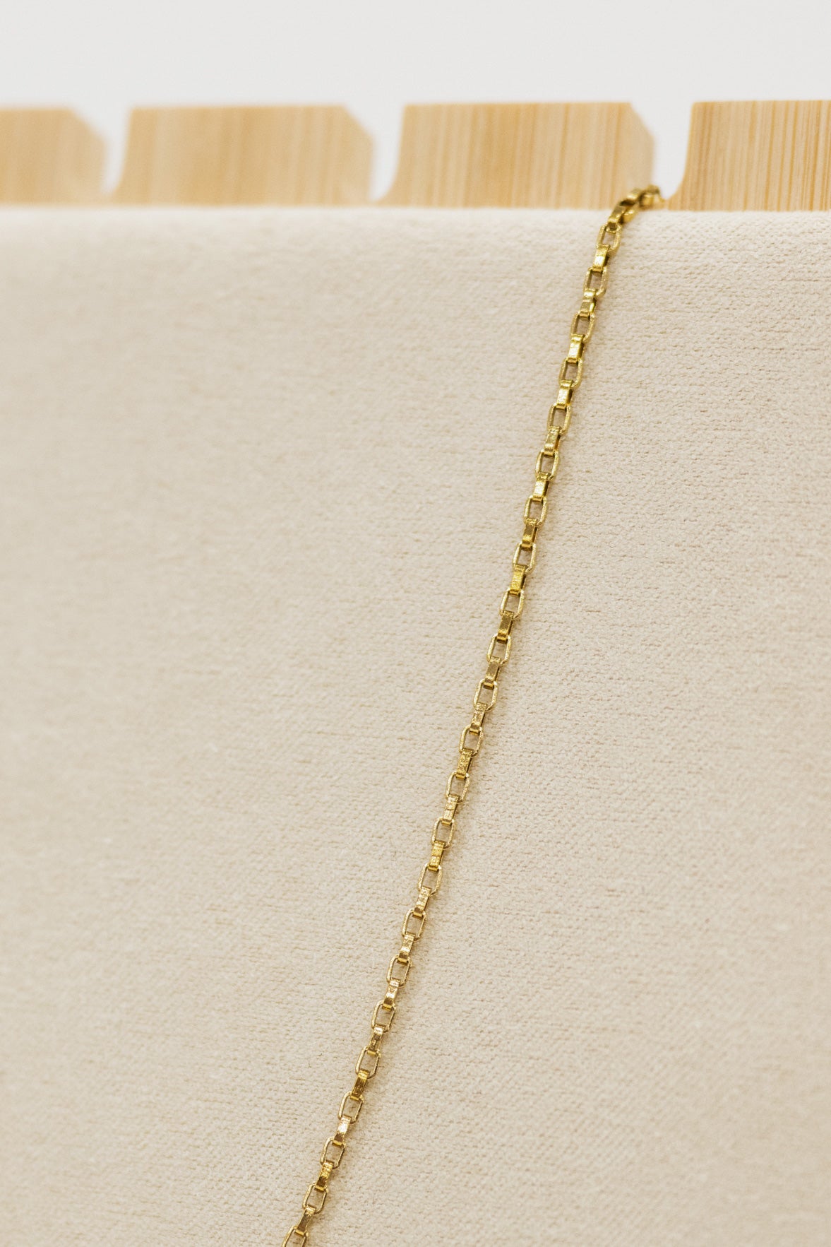 Gold chain necklace on a beige cushion with a wooden stand in the background