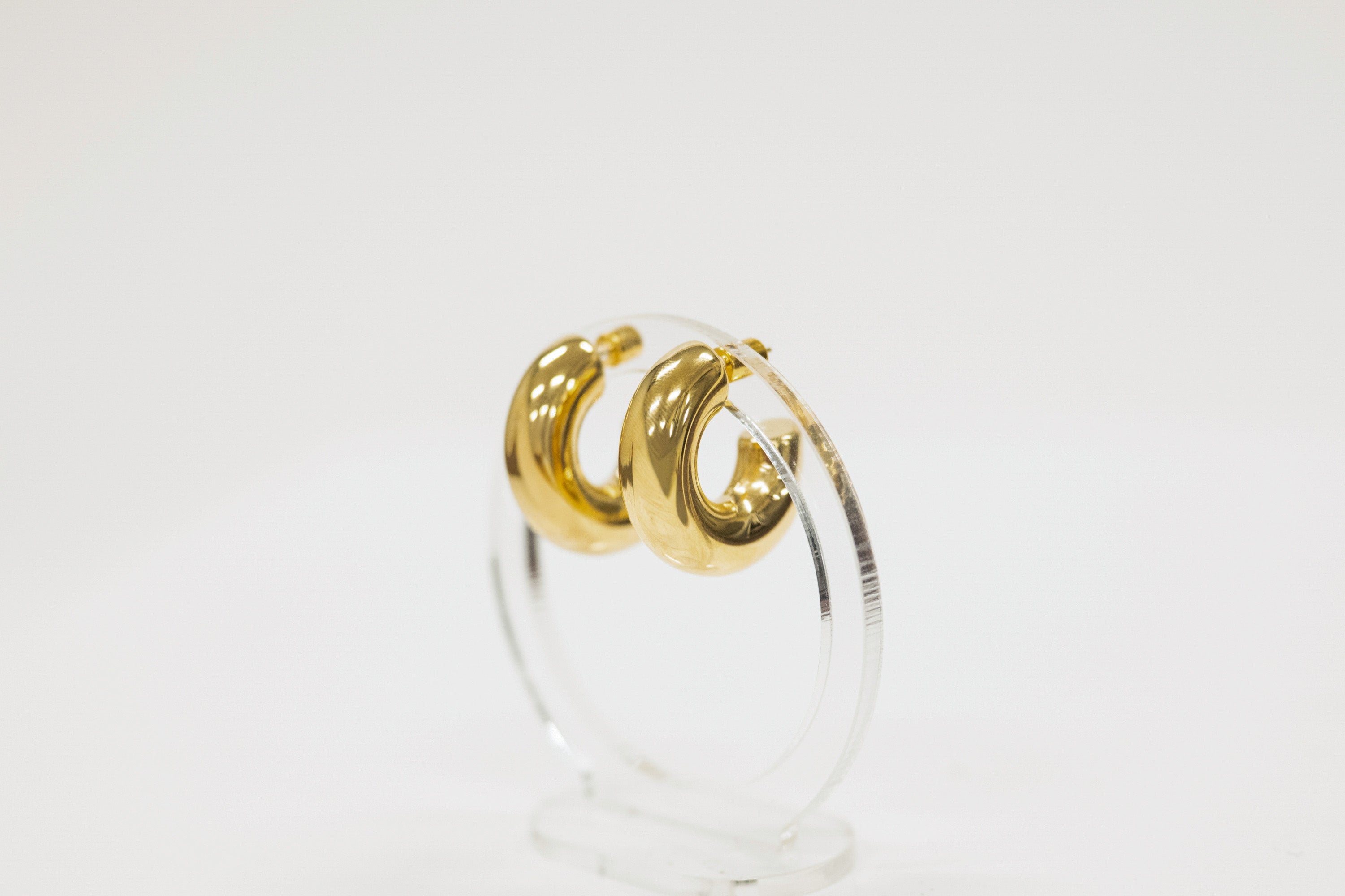 Gold hoop earrings on a clear stand against a white background