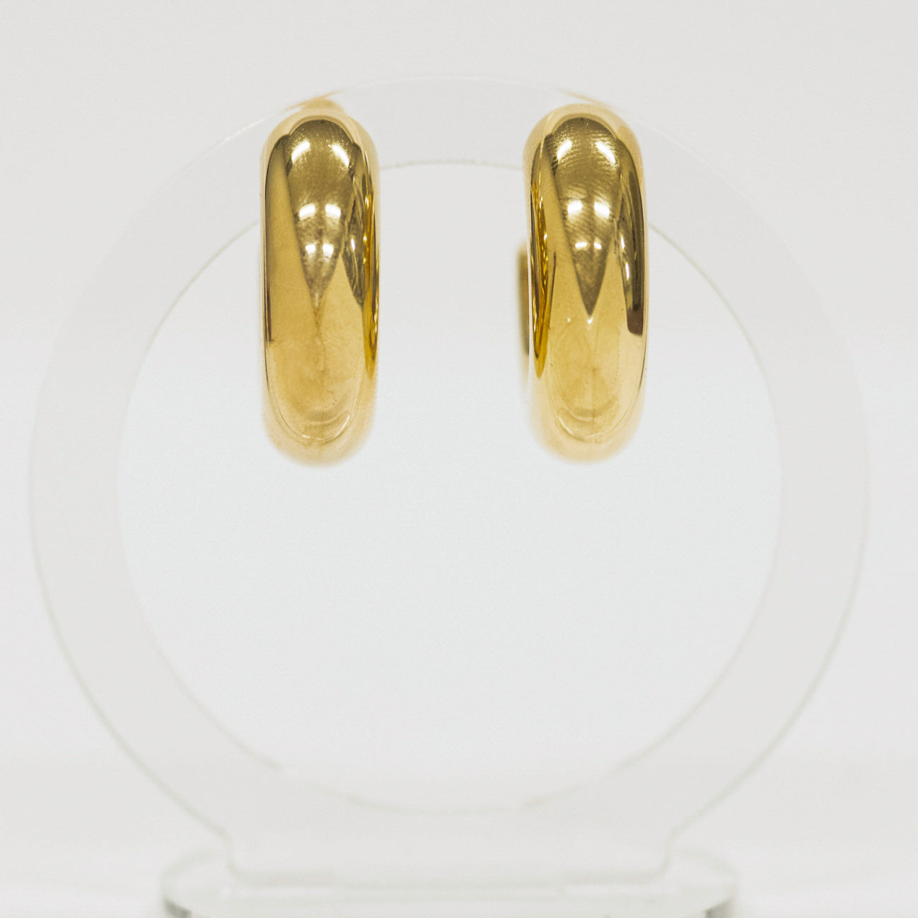 Lightweight gold hoop earrings on a clear stand against a white background