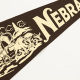 Nebraska-themed decorative banner with a horse, wagon, and cow on a brown background.