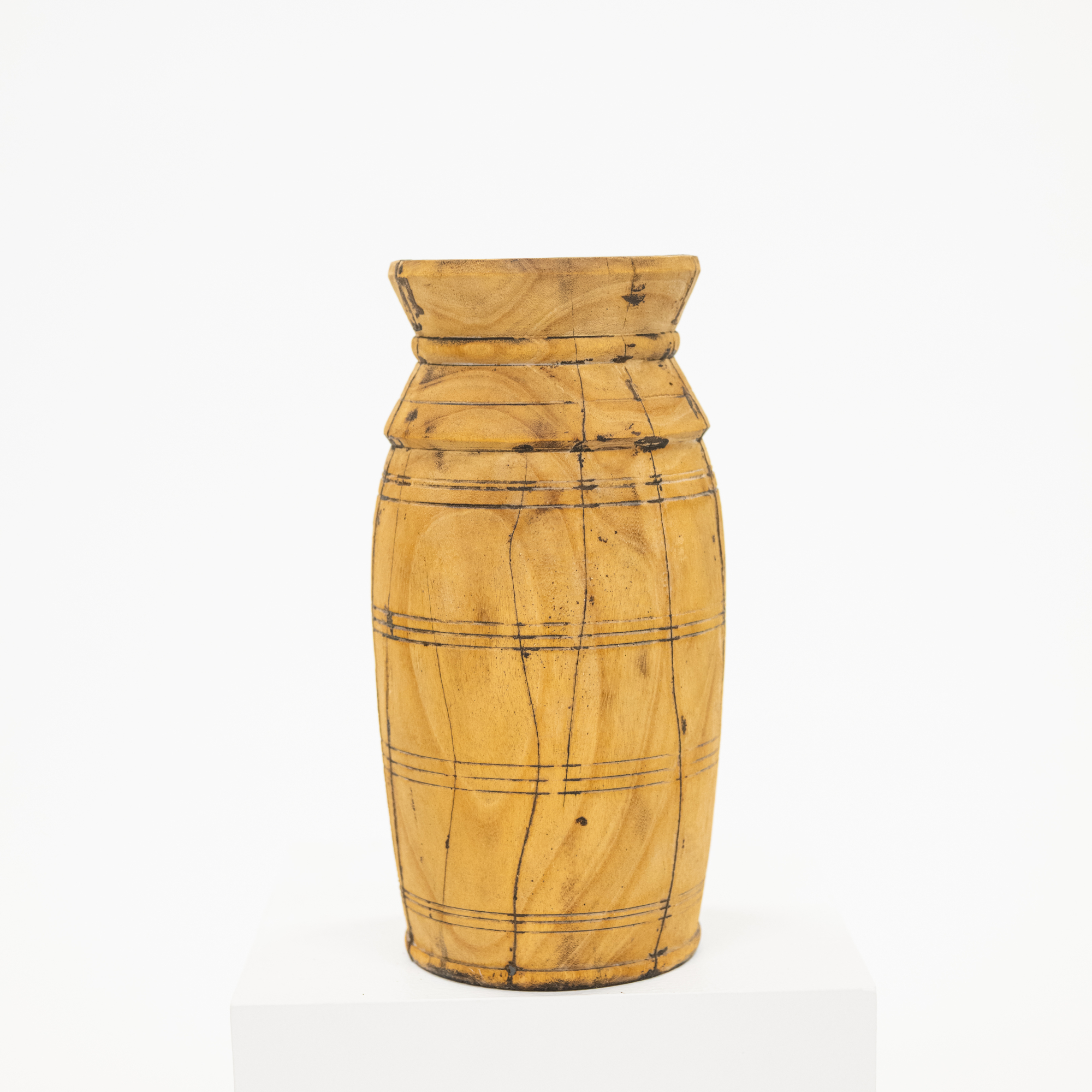 A hand-carved wooden vase with a natural light brown wood grain and dark engraved lines, displayed on a white pedestal against a white background.