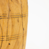 A close-up of a light brown wooden object with dark engraved grid lines, shown against a plain white background.