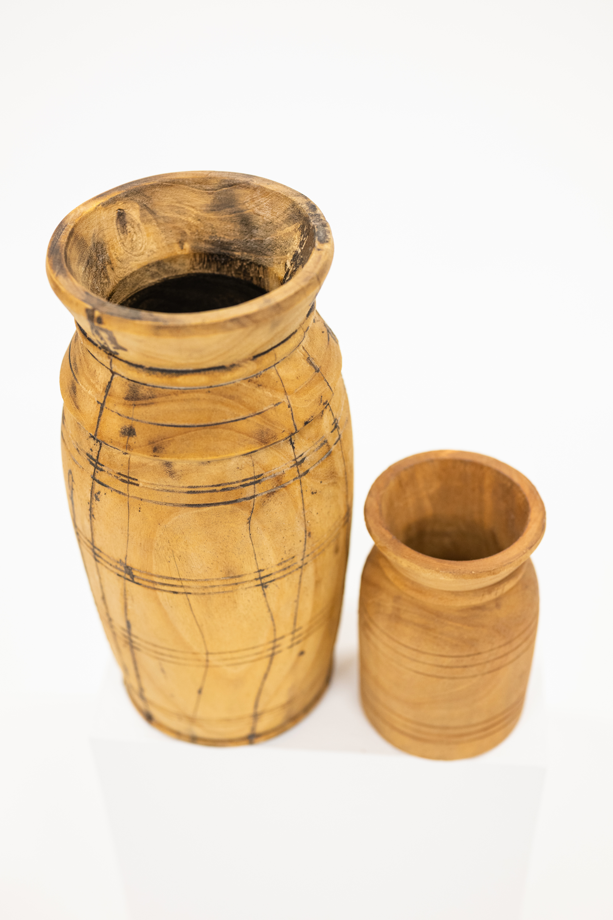 Two handcrafted wooden vases in natural light brown wood tones, featuring one tall vase with dark engraved lines and one smaller matching cup, set against a plain white background.