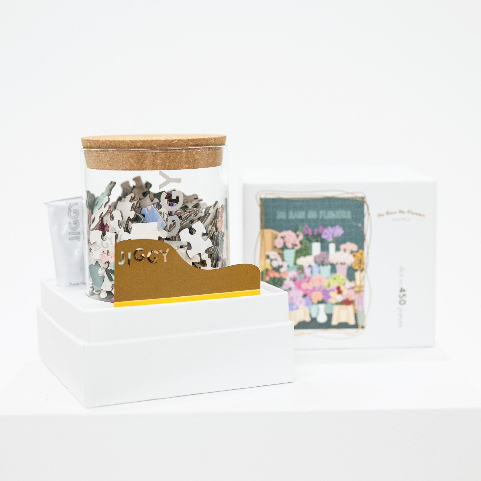 Glass jar of puzzle pieces, with glue and applicator, and a box on a white background
