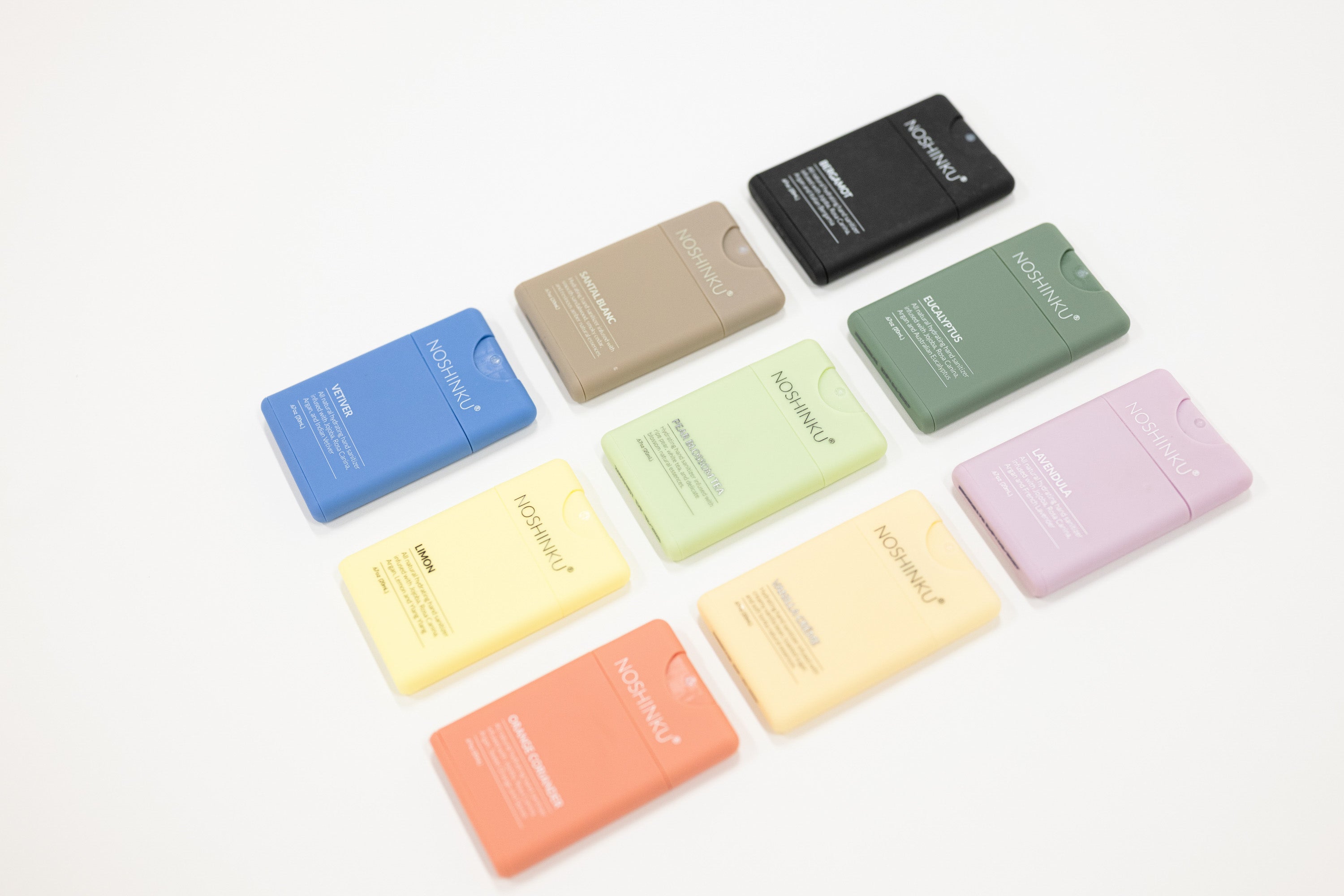 Nine refillable hand sanitizers in assorted pastel and neutral colors, arranged in a loose circle on a clean white background. The bars have a matte finish and a small cutout on one end.