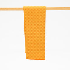 Yellow textured towel hanging on a wooden rack against a white background