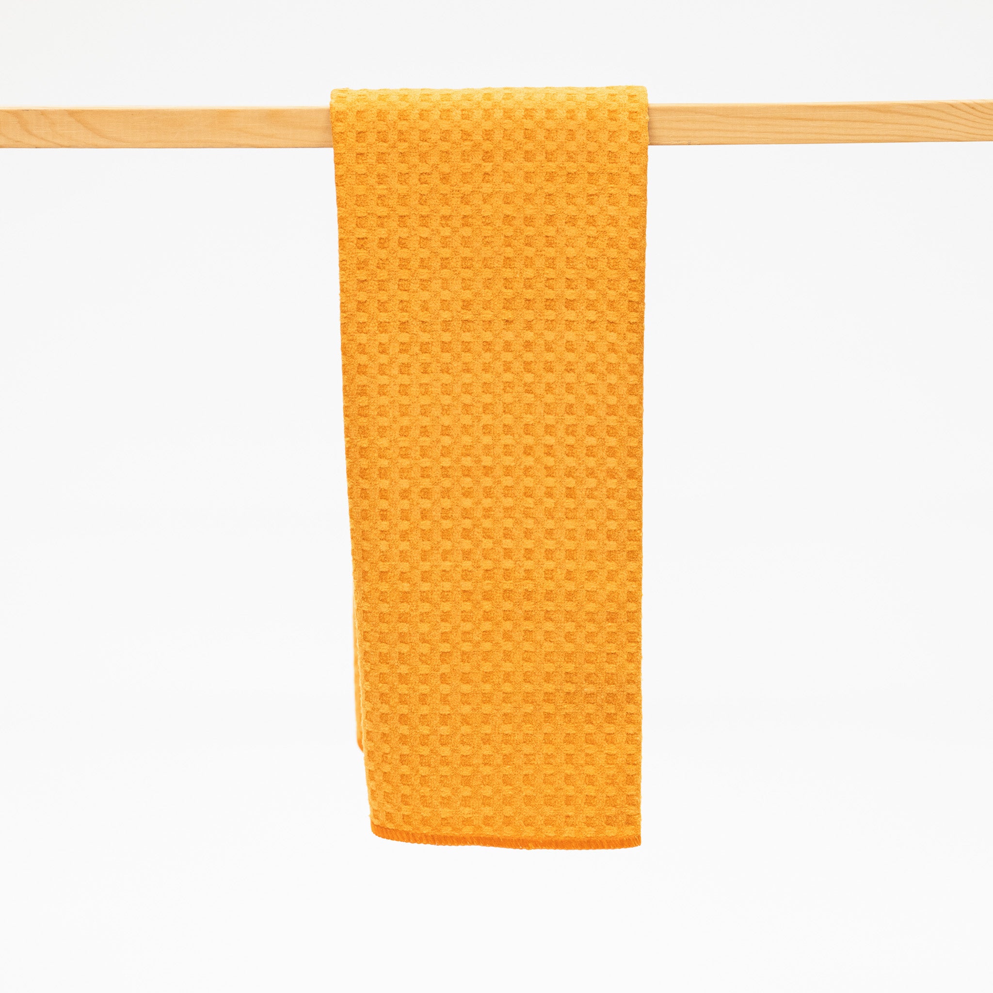 Yellow textured towel hanging on a wooden rack against a white background